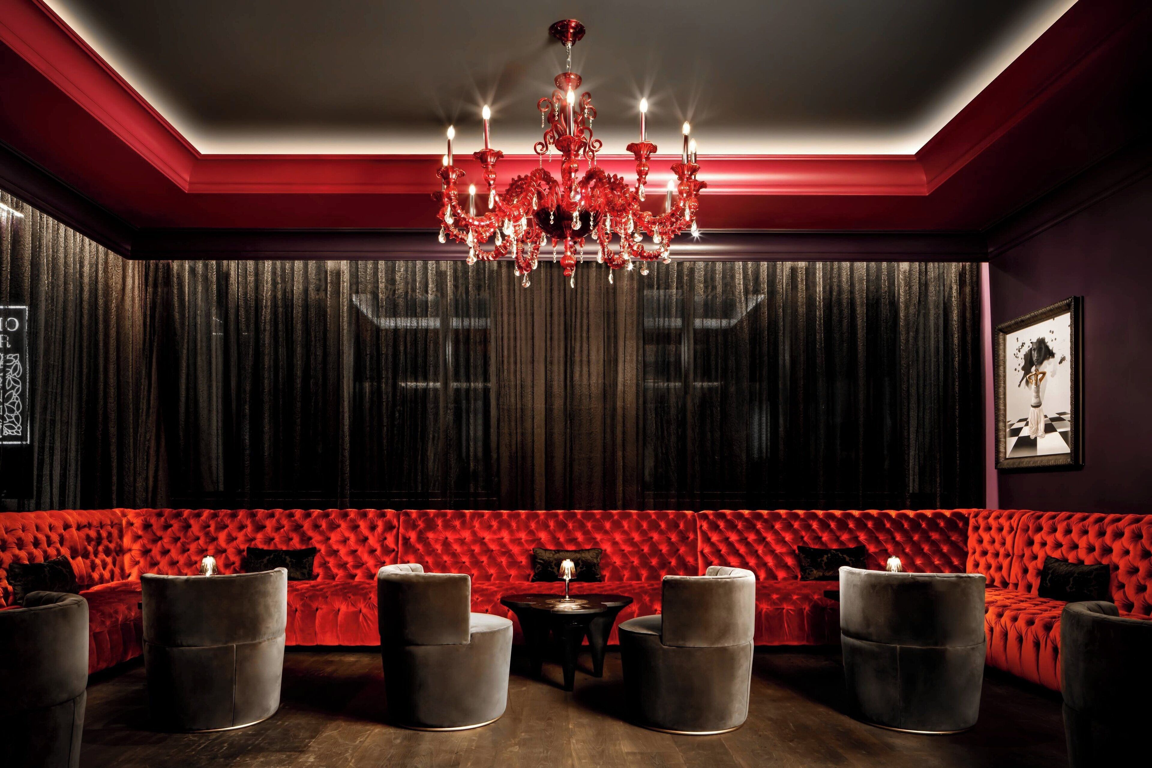 A room with a red velvet sofa, a chandelier, and a dark curtain backdrop.