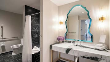 Un baño moderno con lavamanos de mármol, un espejo grande con marco verde azulado y una zona de ducha con azulejos negros.