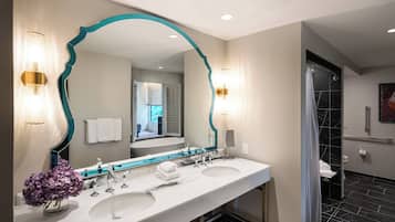 A modern bathroom with dual sinks, a large mirror with teal trim, and a shower area.