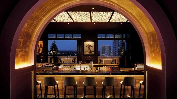 Un espace bar offrant une vue sur la ville la nuit, avec un grand plafond en arc et de nombreux tabourets de bar.