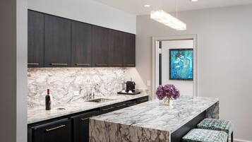 A modern kitchen with dark cabinets, a marble countertop, and a pendant light.