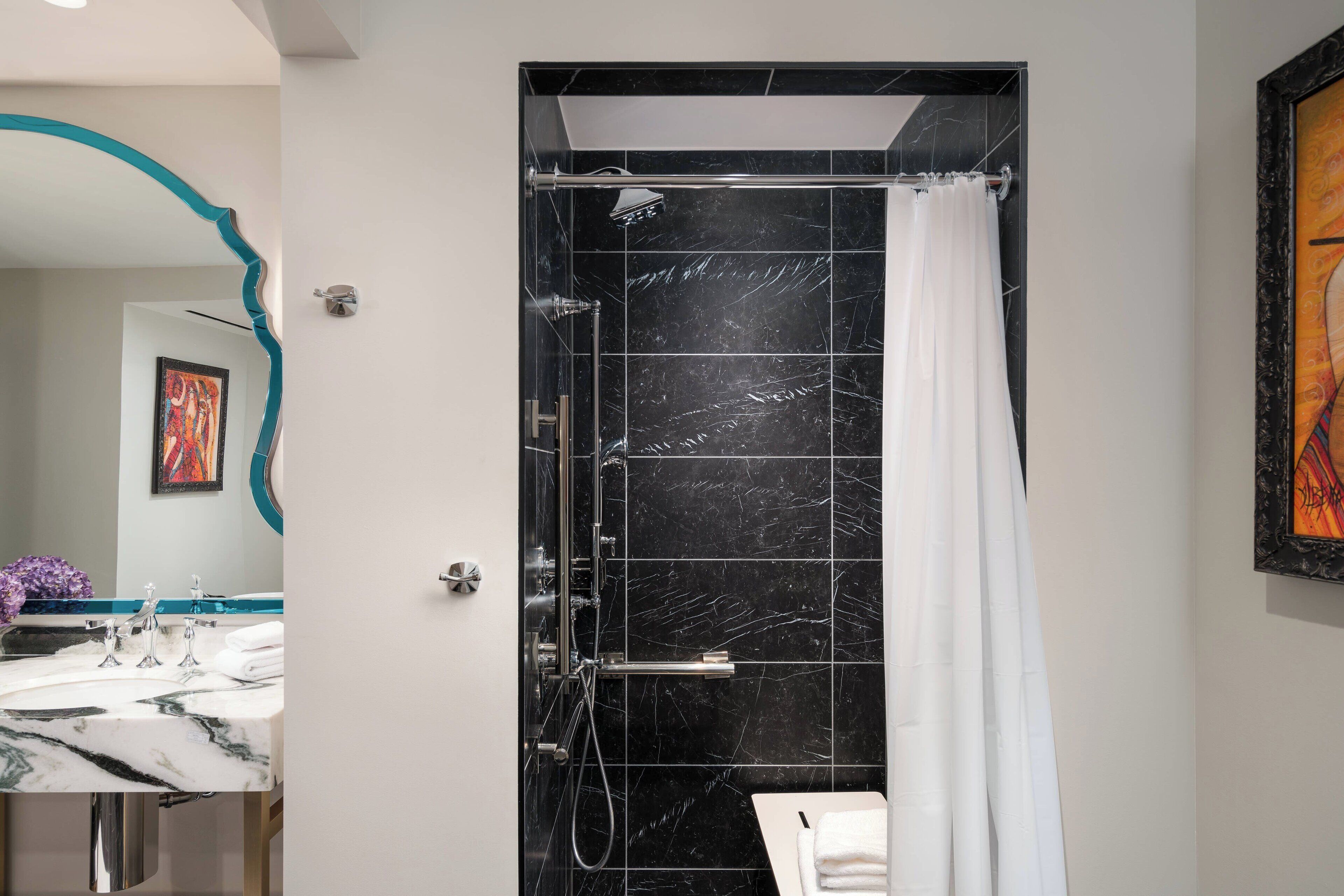 A modern bathroom with a black marble shower, white sink, and a framed artwork on the wall.