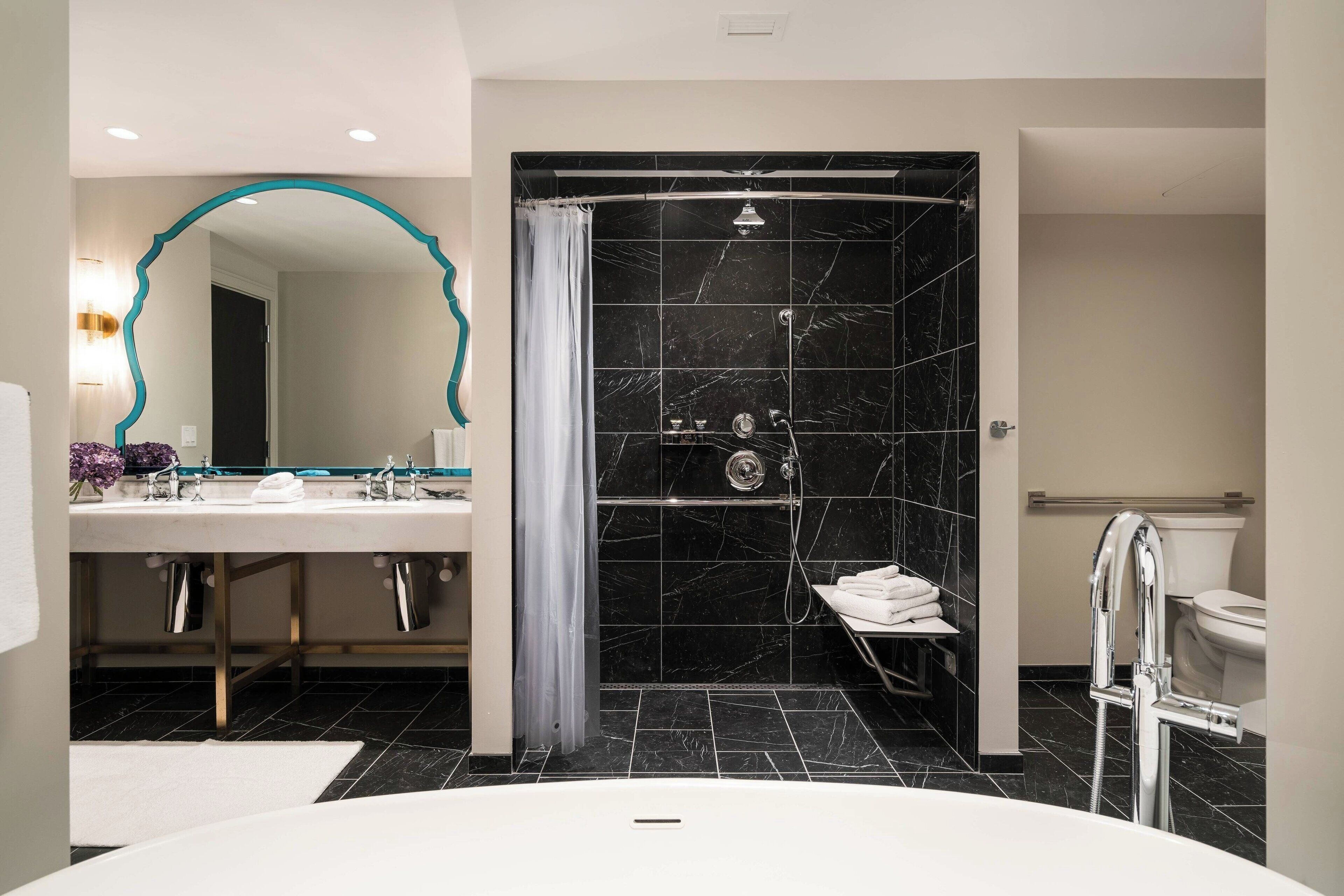 Un baño moderno con una bañera grande, zona de ducha separada con azulejos de mármol negro, tocador con espejo y un inodoro.