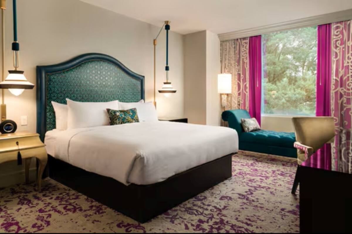 Ein Hotelzimmer mit einem großen Bett, zwei Nachttischen, einem Schreibtisch, einem Sessel und einem fenster mit Vorhängen.