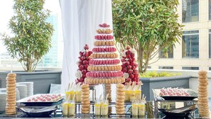 Une table de buffet où sont présentés des macarons, des beignets et d’autres pâtisseries, disposés sur des plateaux.