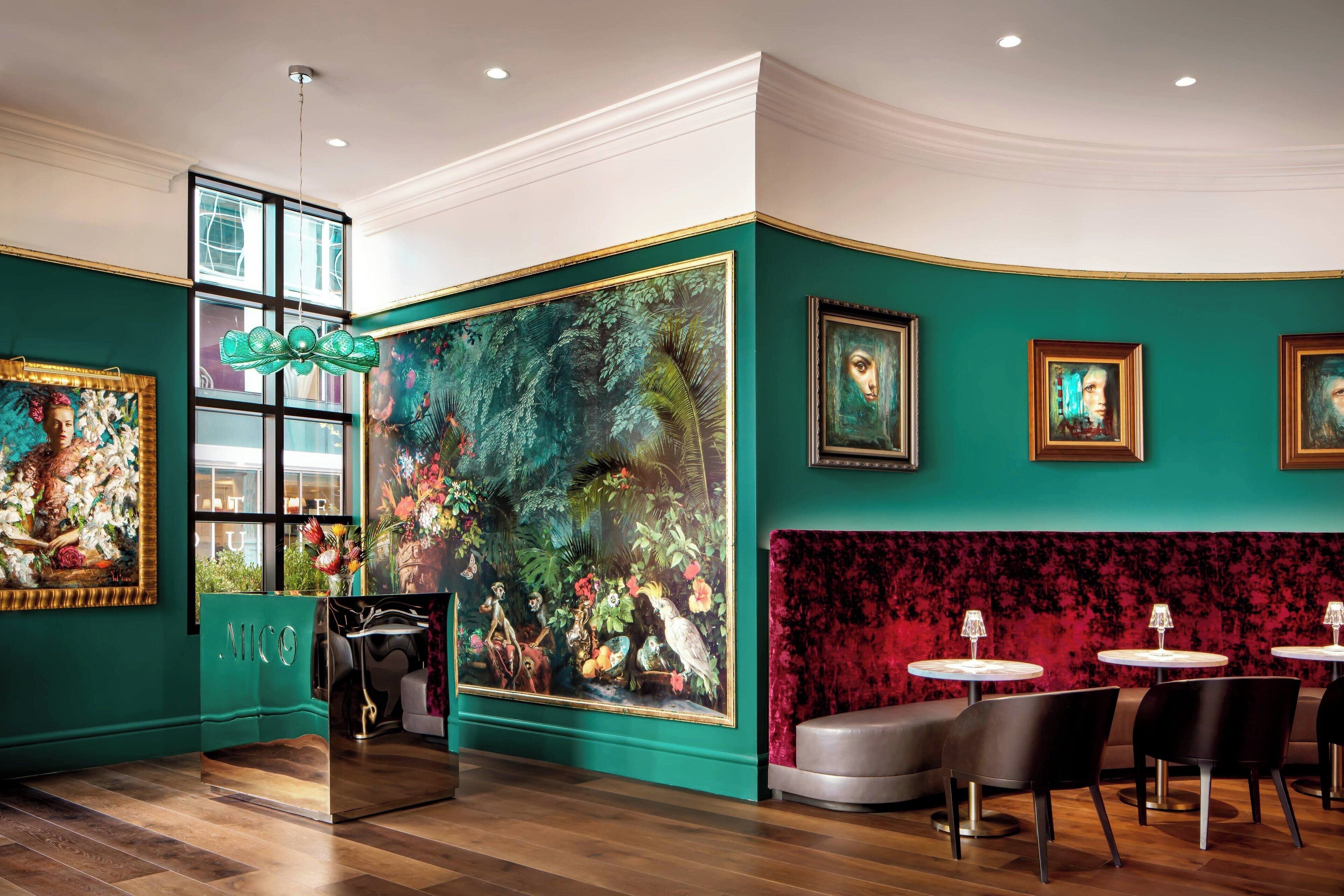 A restaurant with a green wall, large paintings, and a red velvet booth.