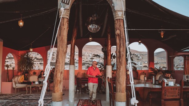 A spacious room with a high ceiling, wooden pillars, and a patterned rug. - Nomads Hotel Petra (Wadi Musa)