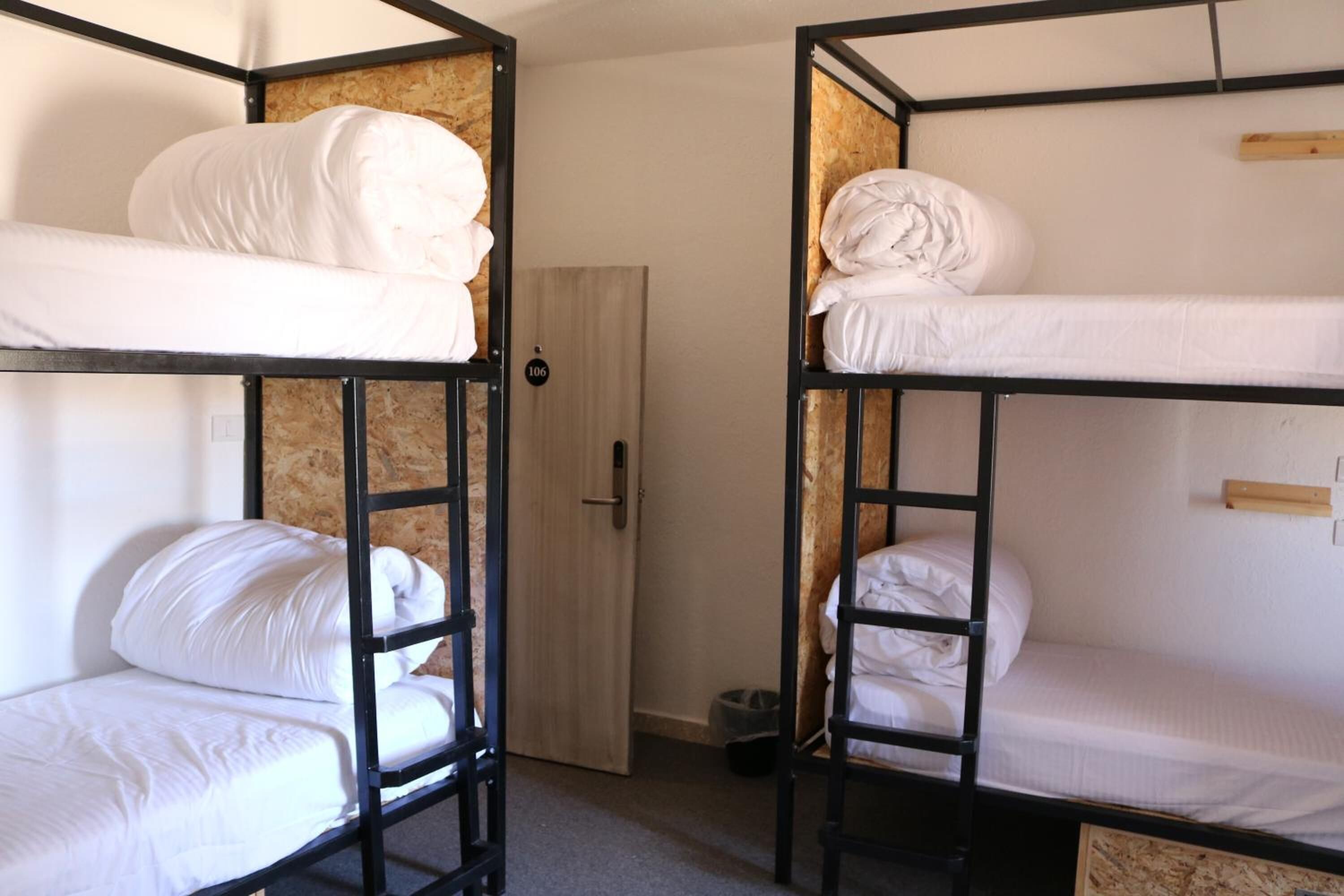 Une chambre avec un lit superposé, deux lits, une porte et une poubelle.