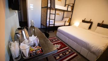 Quarto de hotel com beliche, uma cama de solteiro, mesa com bandeja de lanches, uma garrafa e copos.