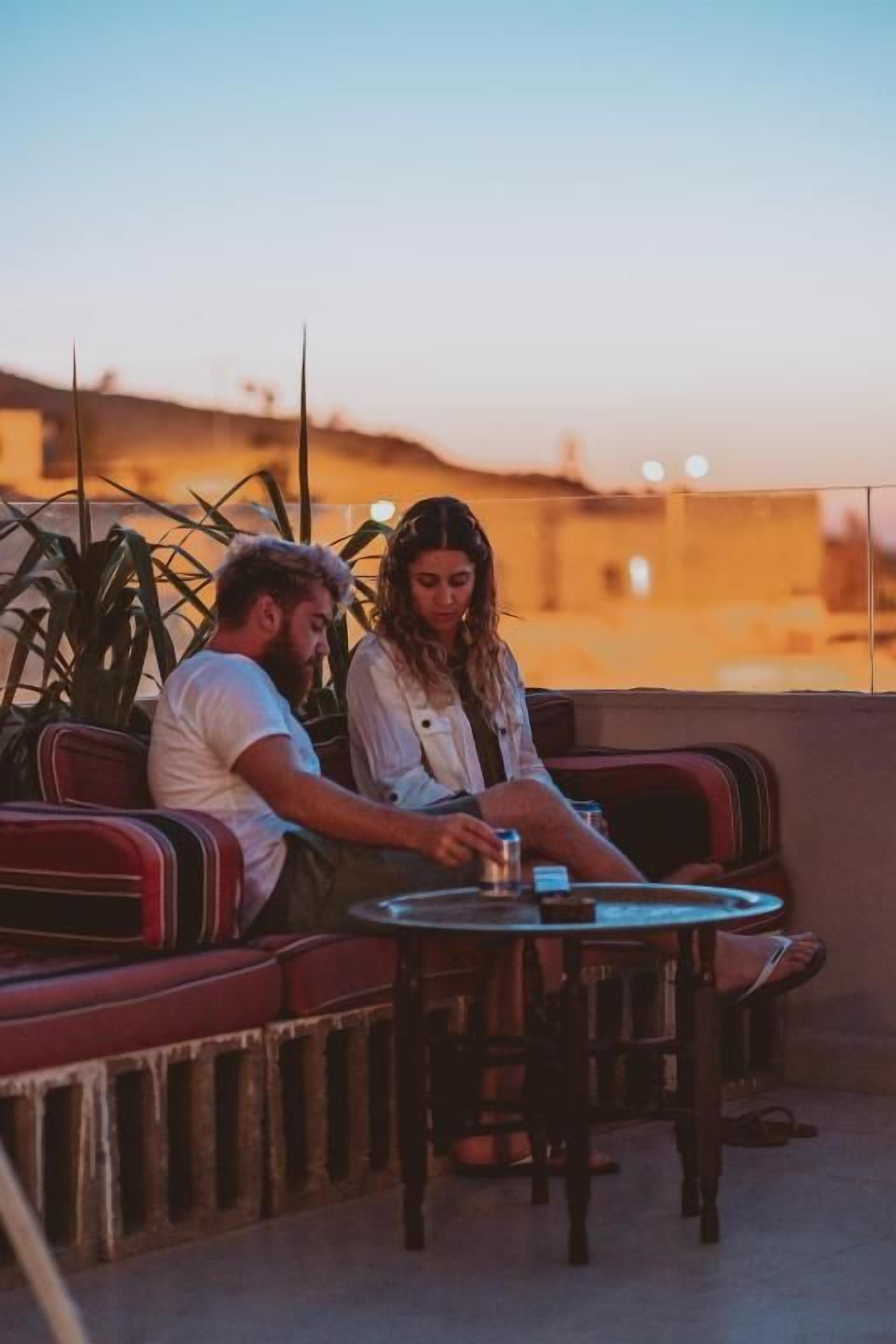 A couple seated at a small round table on a rooftop terrace with a view of the cityscape.