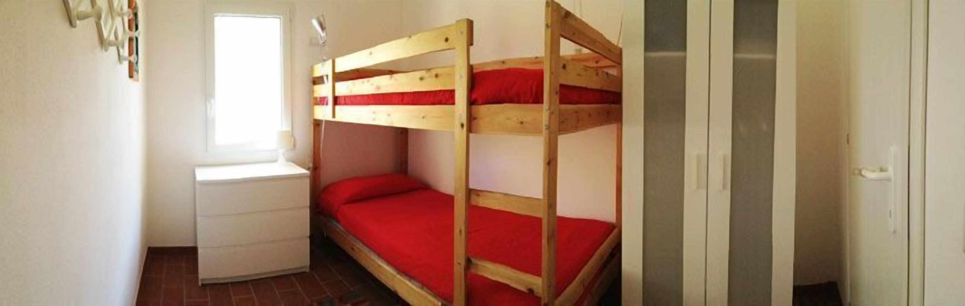 A small, compact room with a bunk bed and a single bed, a small dresser, and a window.