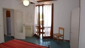 Una habitación con cama, ventilador de techo, puerta, una silla y ventana con cortinas.