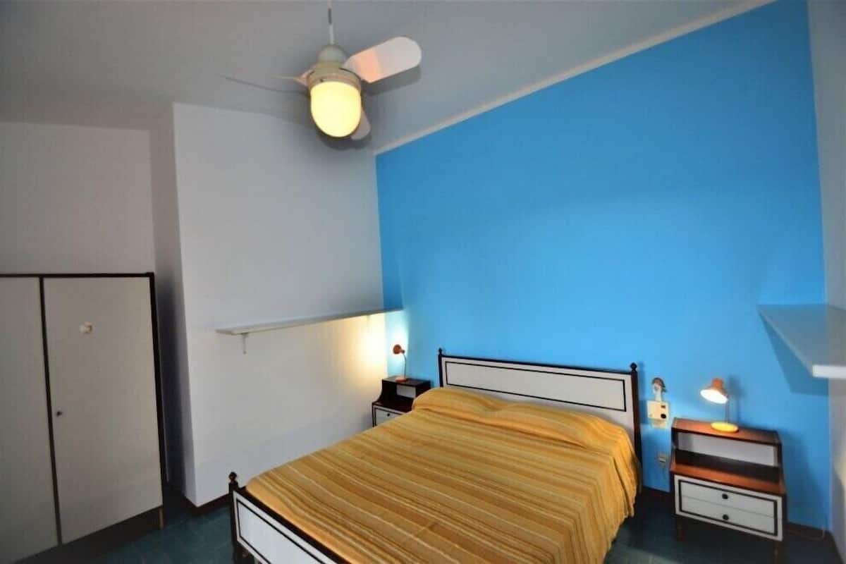 A bedroom with a bed, a nightstand, a bedside lamp, a ceiling fan, and a wardrobe.