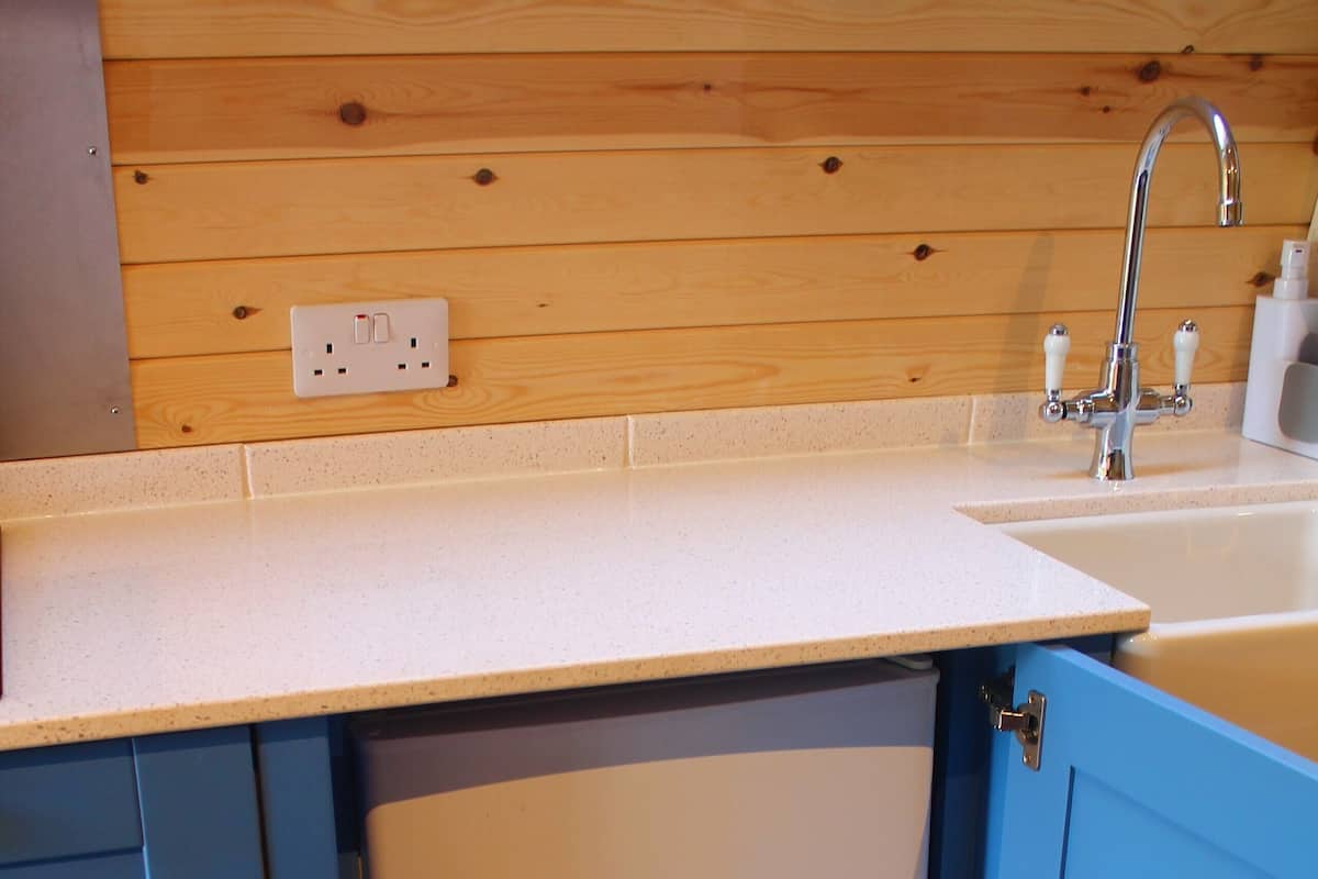 Eine Küche mit Holzwandverkleidung, einer weißen Arbeitsplatte, einem Zweitür-Kühlschrank und einem Spülbecken mit Armatur.
