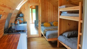 A compact wooden cabin with a kitchenette, a bunk bed, and a door leading to an outdoor area.