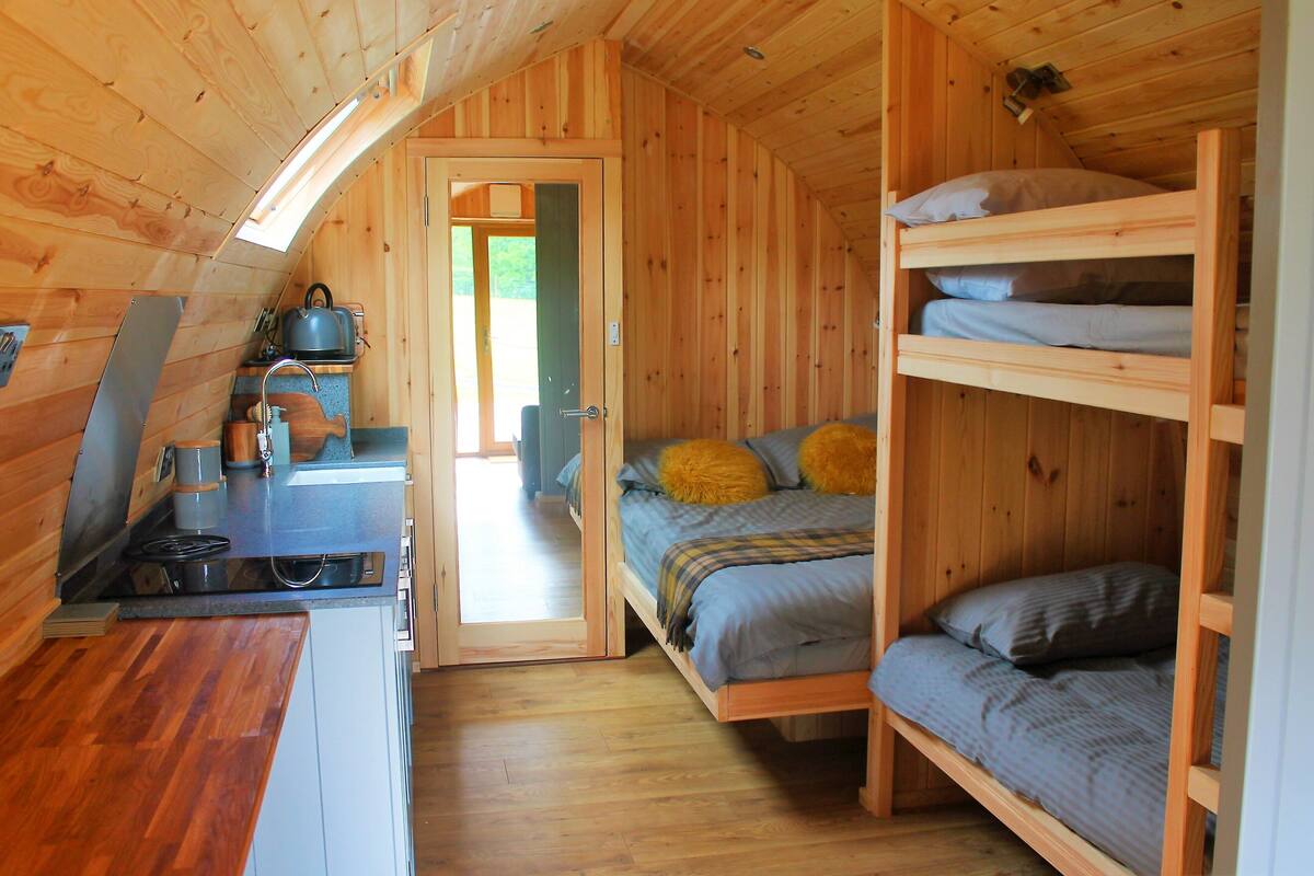 Eine kompakte Holzhütte mit Küchenzeile, Etagenbett und einer Tür zu einem Außenbereich.