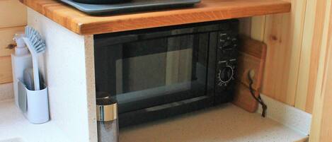 A compact kitchenette with a microwave, toaster, and kettle on a wooden countertop.