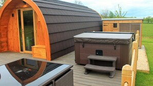 A wooden cabin with a curved roof, a hot tub, and a deck with outdoor furniture.