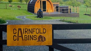 A cabin with a curved roof, a wooden door, and a sign indicating it is part of the Cairnfold Cabins.
