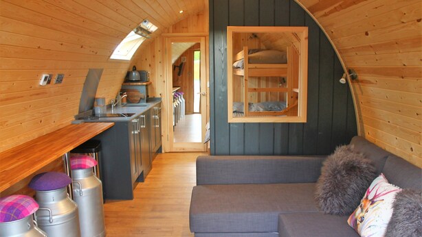 A compact, wooden interior with a kitchenette, a sofa, and a window.