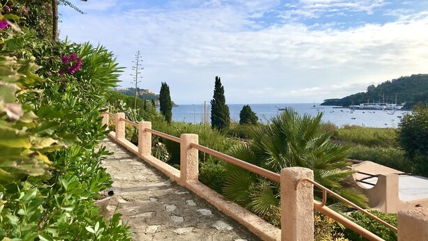 A stone staircase leading to a terrace with a view of the sea and boats. - Il Portolano (Porto Azzurro)