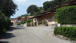 A residential street with houses, a paved road, and greenery. - Il Portolano (Porto Azzurro)