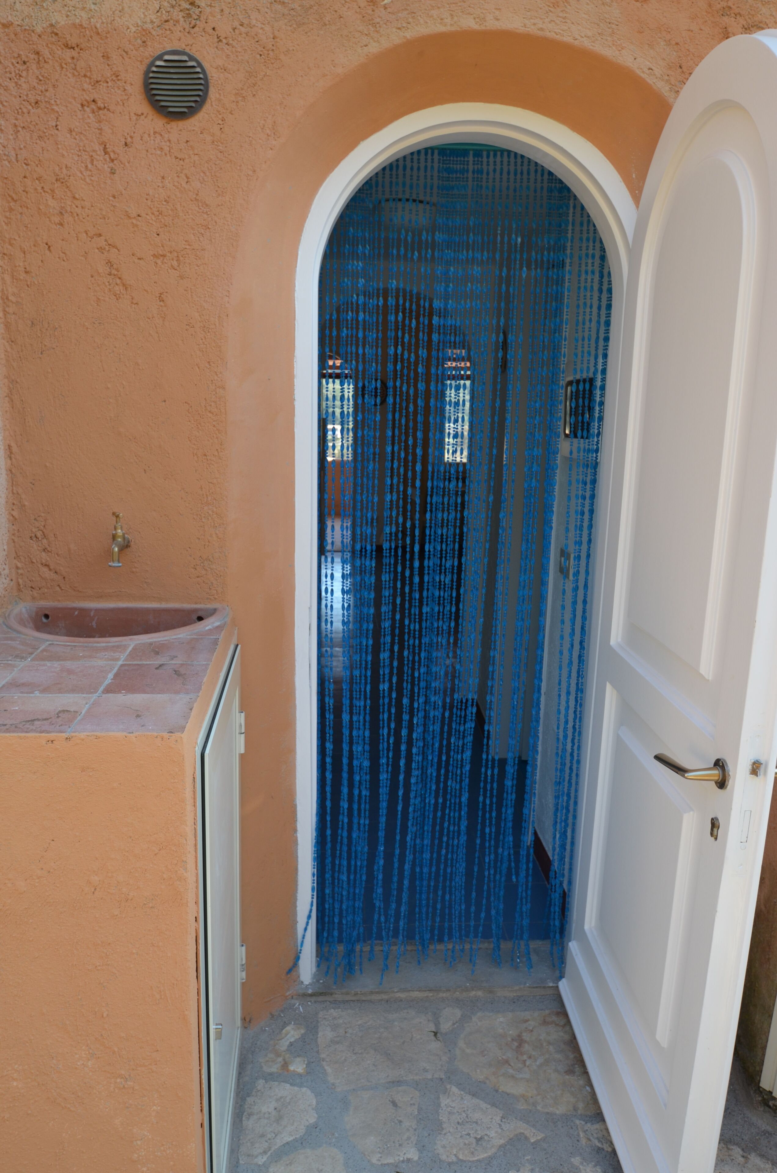 A narrow doorway with a blue curtain, a white door, and a stone floor.