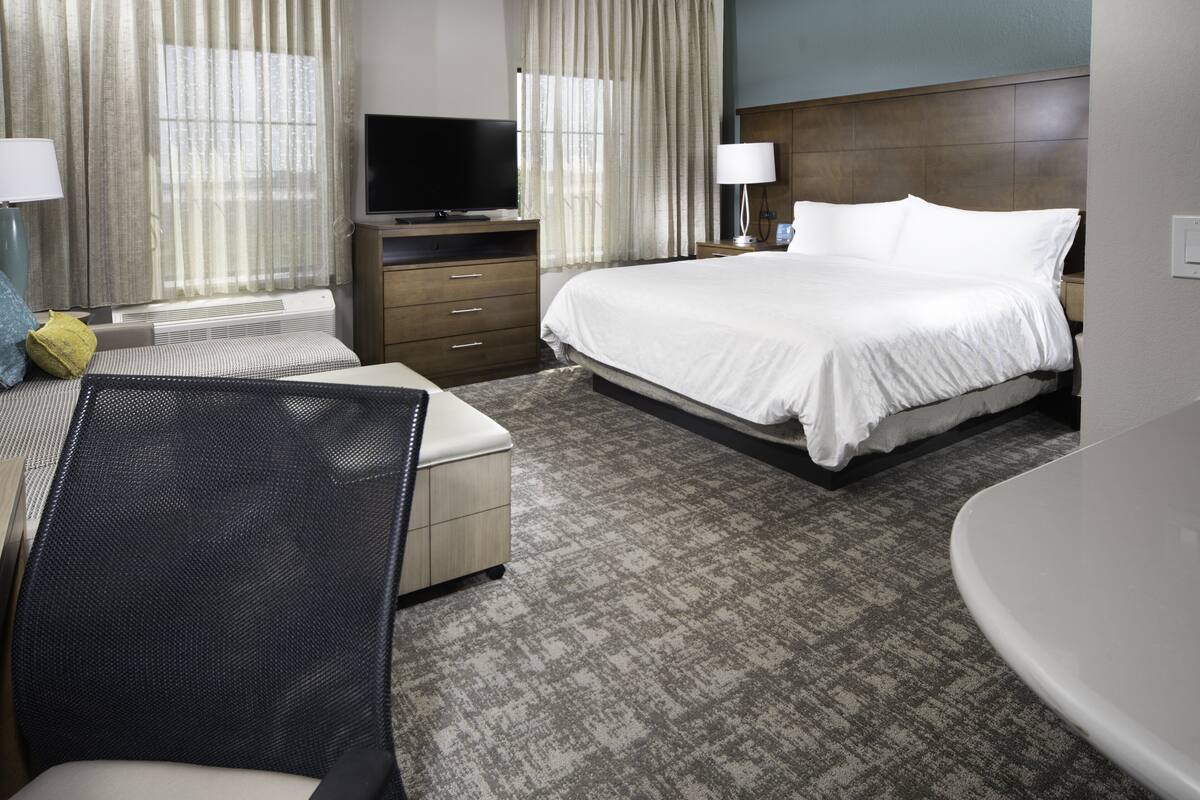 A hotel room with a bed, a desk, a chair, a television, and a bedside table with a lamp.