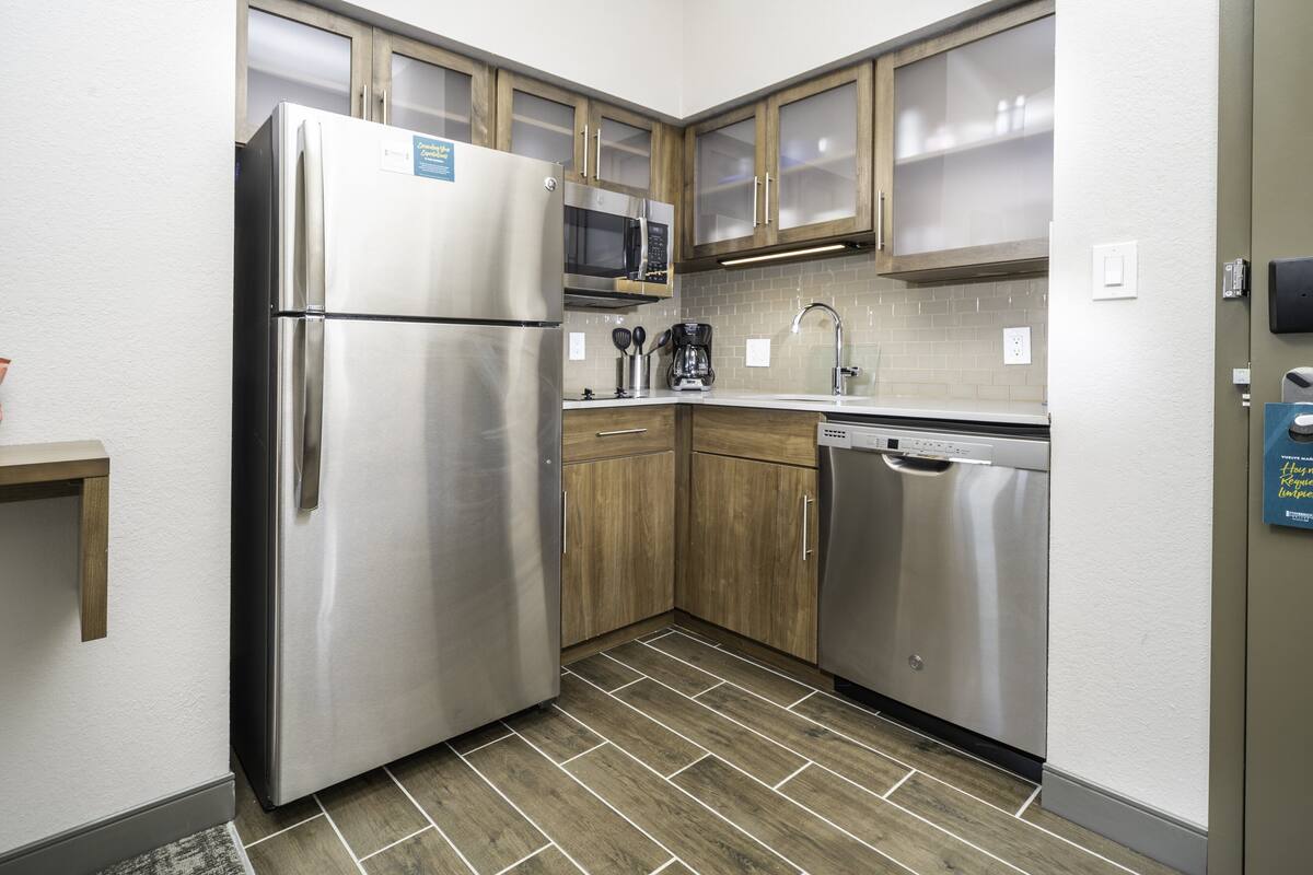 A compact kitchen with a stainless steel refrigerator, a microwave, wooden cabinets, and a dishwasher.
