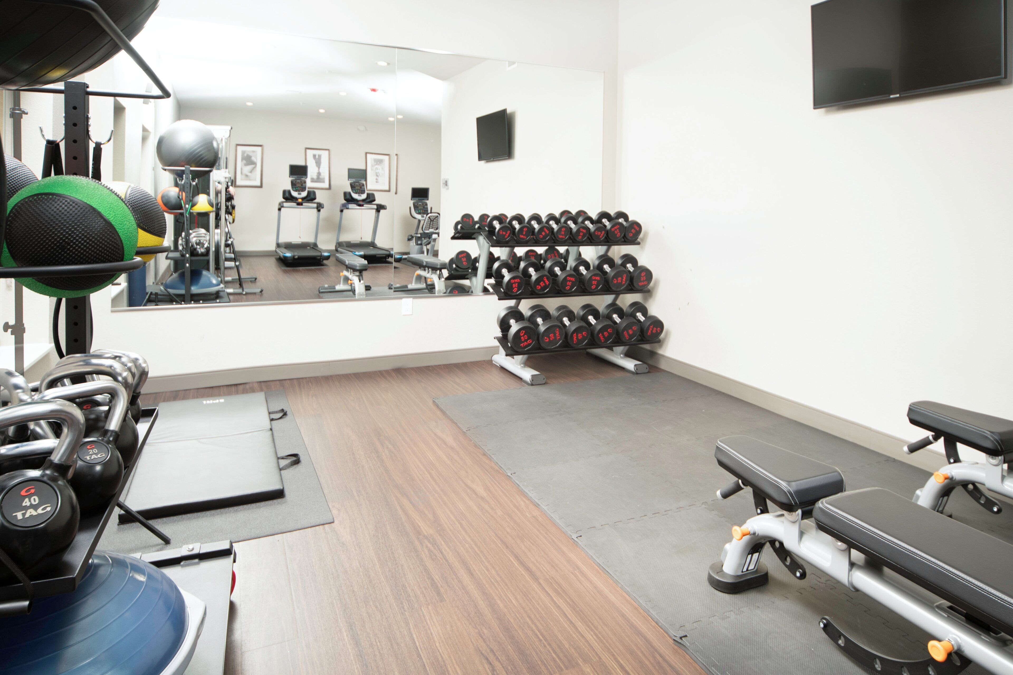 Un gimnasio con equipo de ejercicio, una banca y un televisor en la pared.