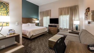 A hotel room with a bed, a sofa, a desk with a lamp, a TV, and a window with curtains.