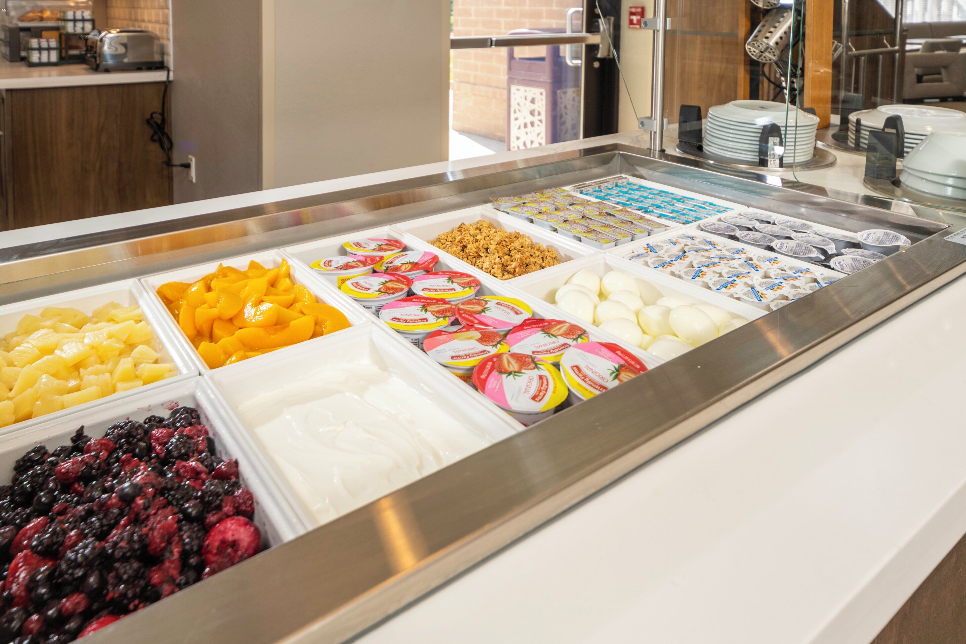 Buffet de café da manhã com diversas opções de alimentos, incluindo frutas, iogurte e granola.