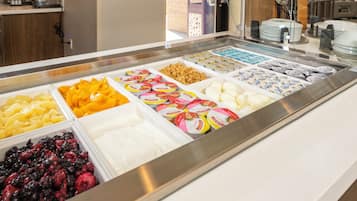 Buffet de café da manhã com diversas opções de alimentos, incluindo frutas, iogurte e granola.