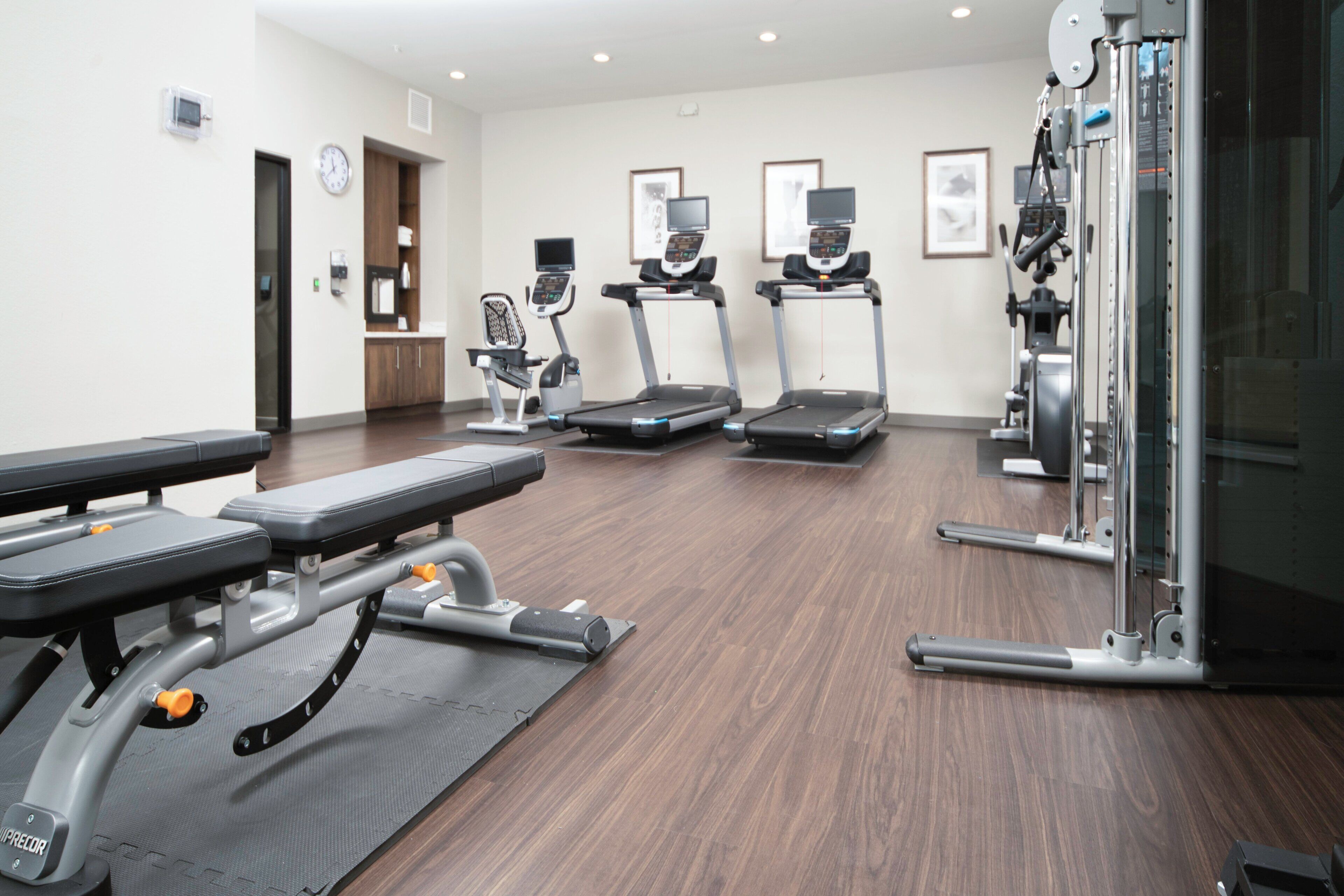 Un gimnasio con cintas de correr, una prensa de banca y una máquina de pesas.