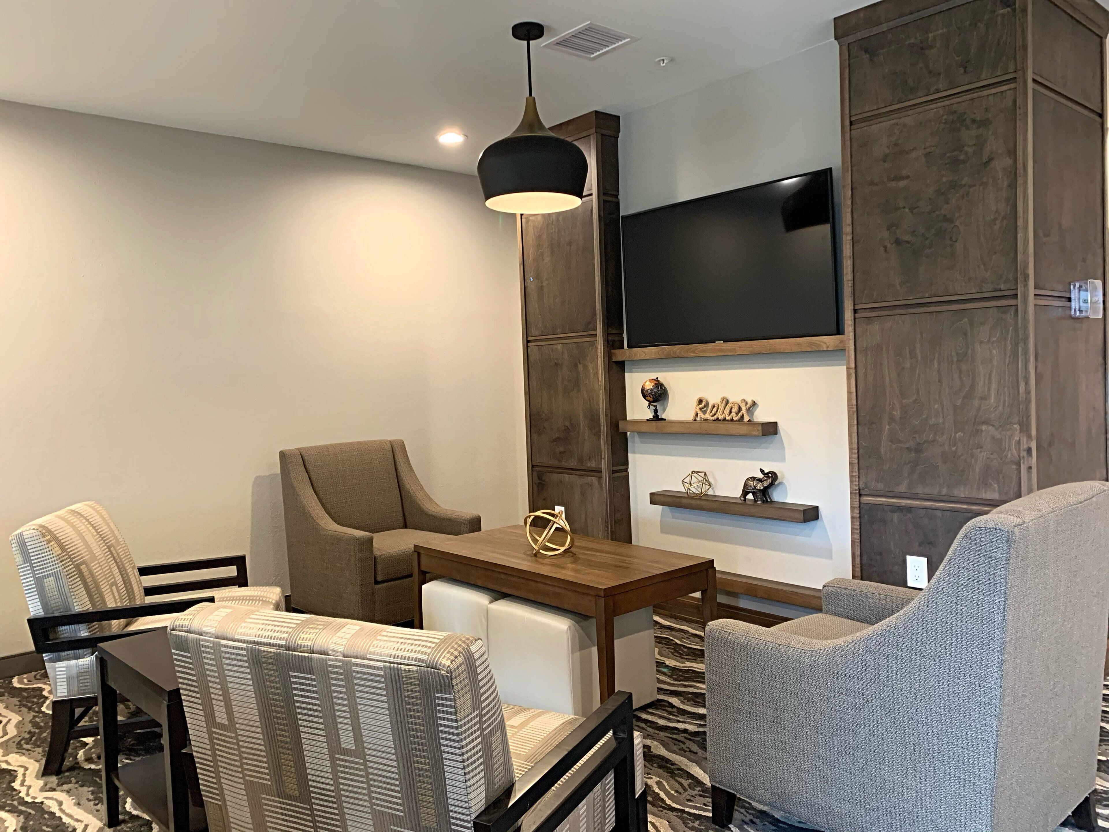 Una sala de estar moderna con un sofá, sillones, una mesa de centro y un televisor montado en una pared de madera.
