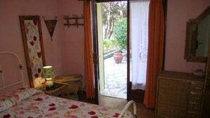 A bedroom with a bed, a nightstand, a lamp, a dresser, and a sliding glass door leading to an outdoor area. - Silvia (Capoliveri)