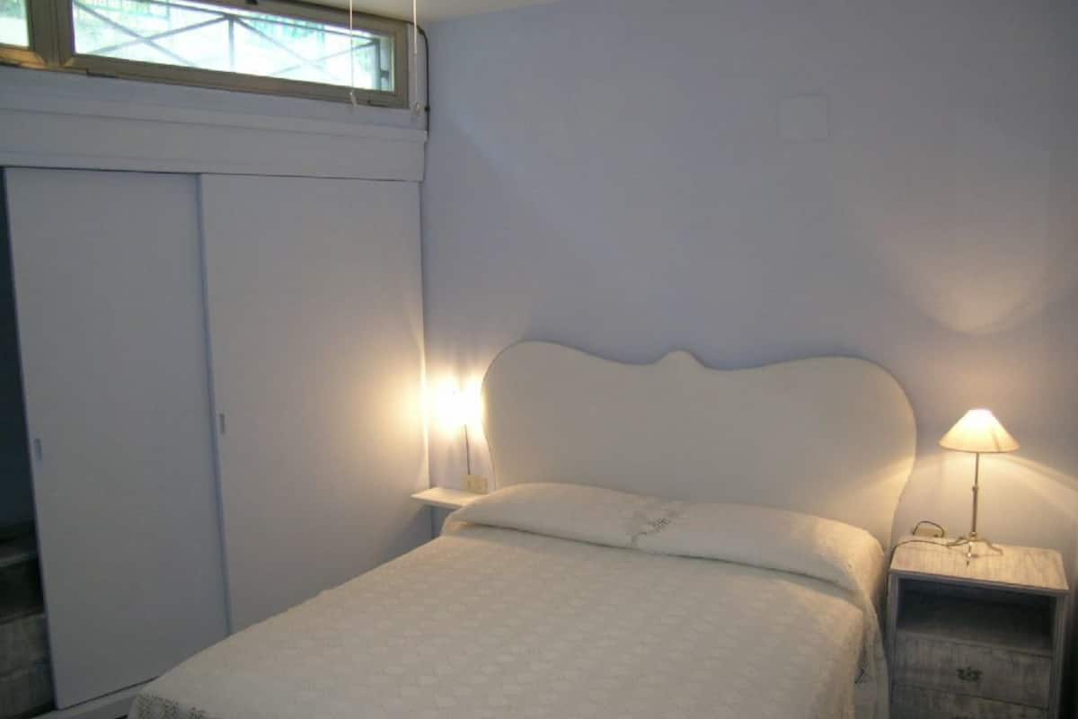 Un dormitorio con cama, mesitas de noche, armario y ventana.