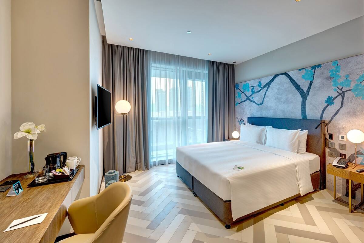A hotel room with a large bed, a desk with a chair, a TV, and a painting on the wall.