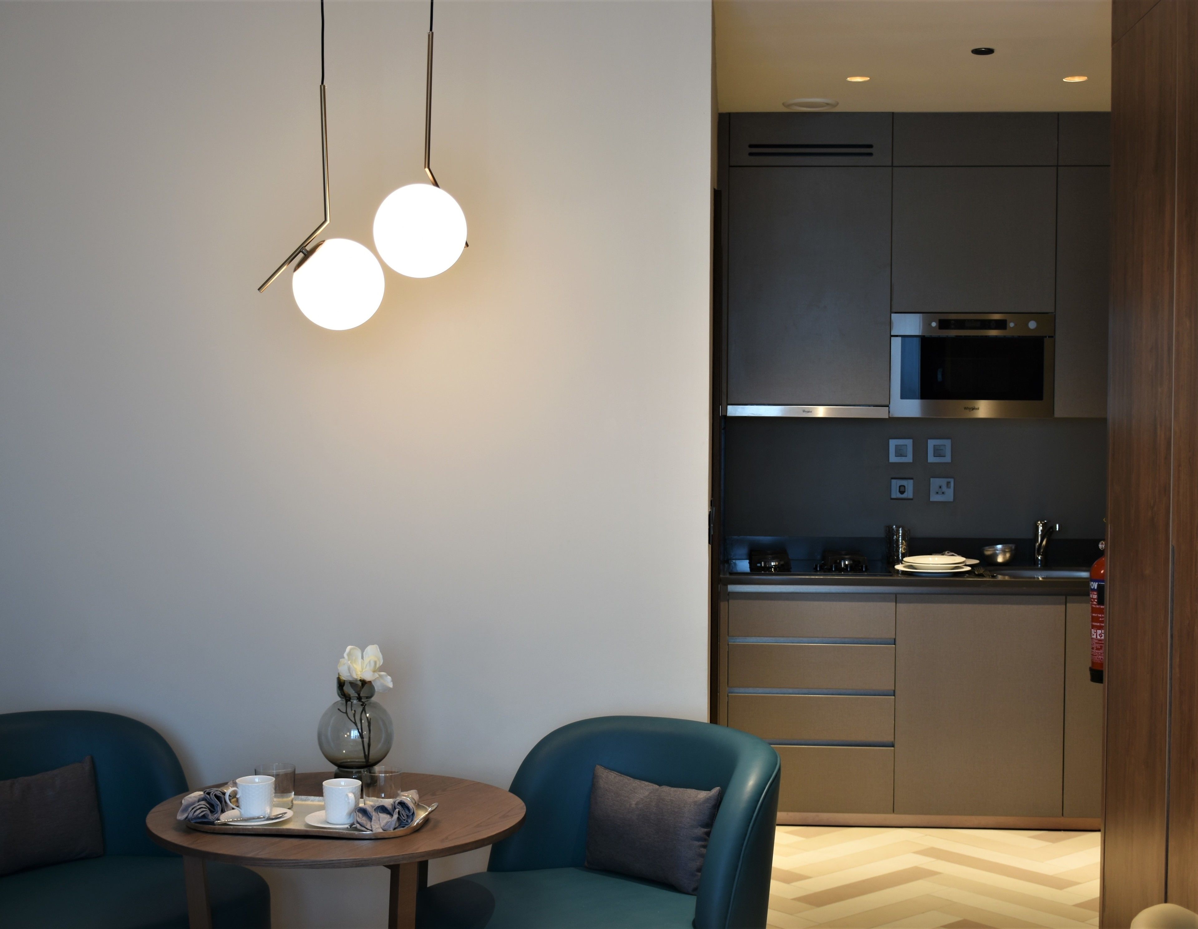 Een moderne keuken met roestvrijstalen apparatuur, een eethoek met een ronde tafel en twee blauwe stoelen.