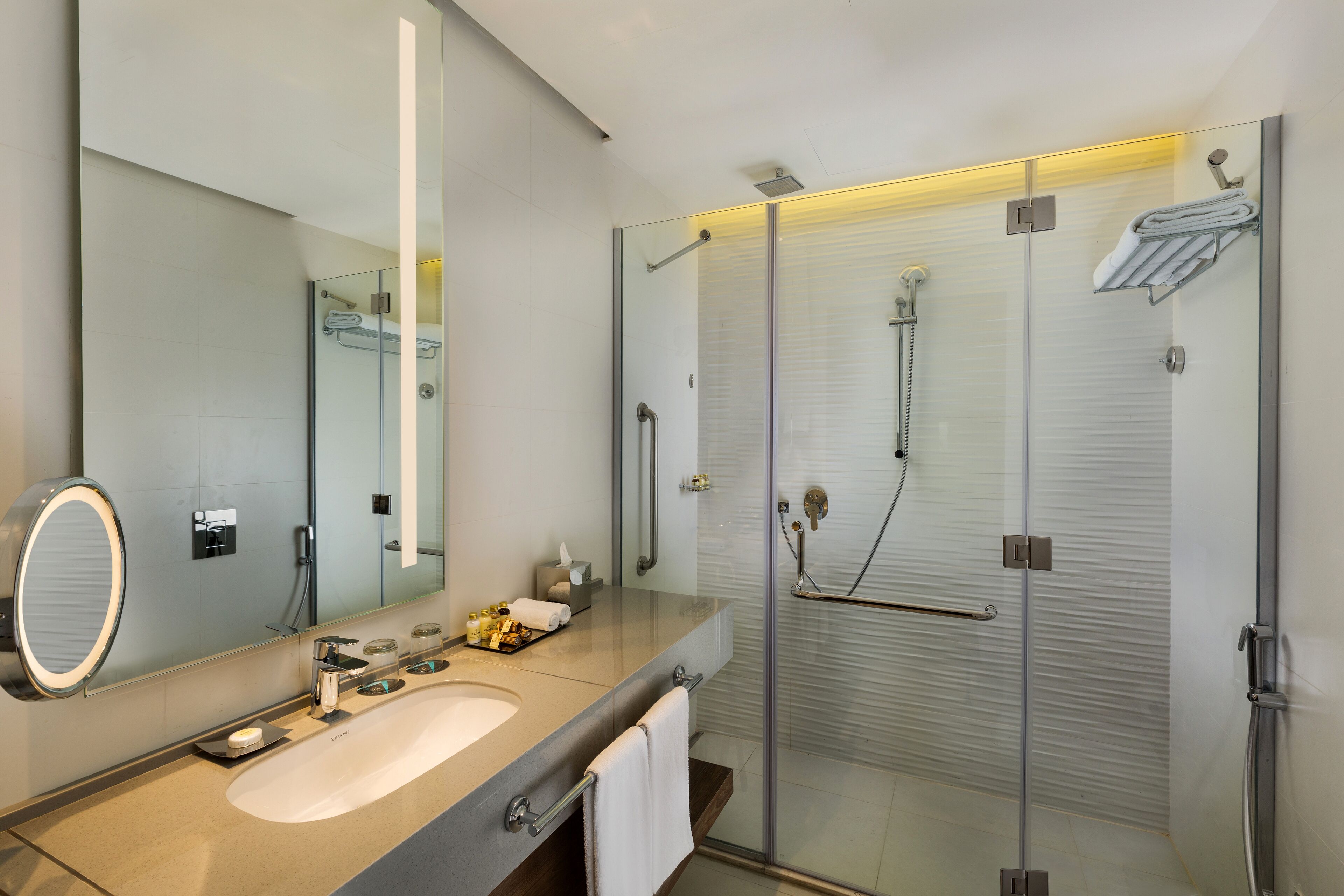 A modern bathroom with a glass-enclosed shower, a large mirror, and a vanity with a sink and towel rack.