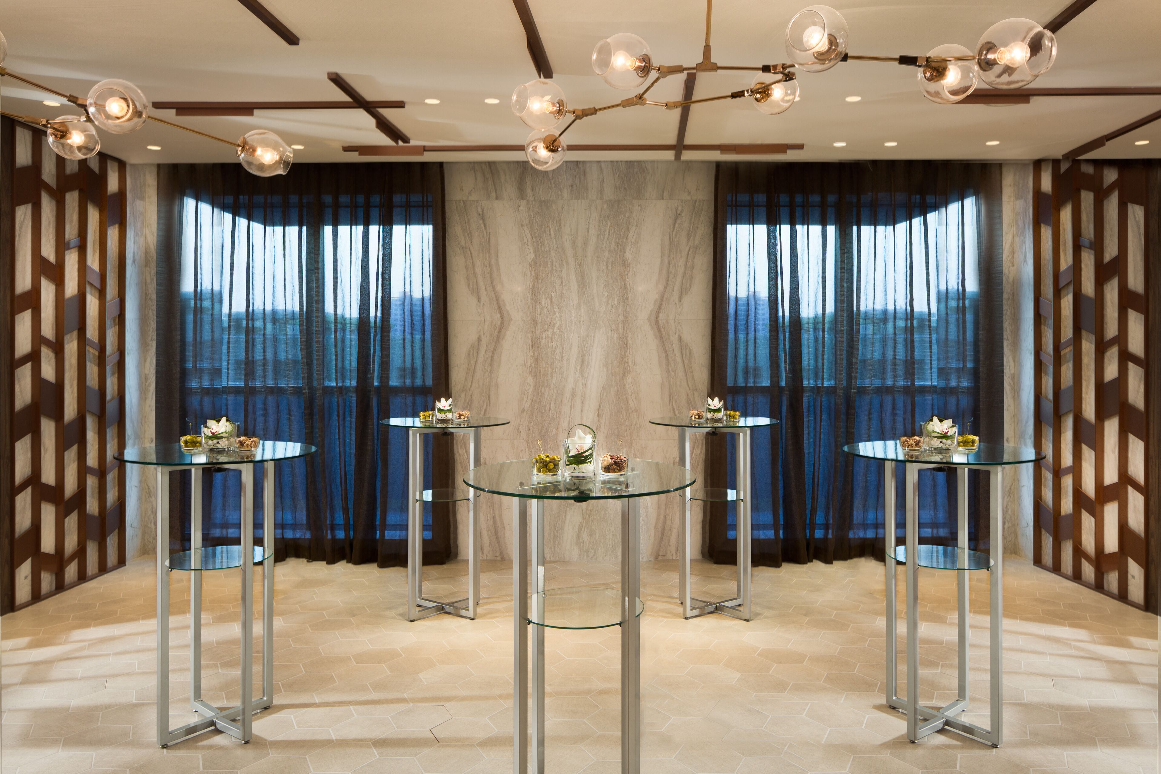 A modern room with three glass-top tables, a decorative ceiling light, and a view of the mountains through large windows.