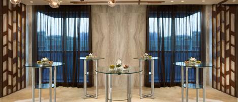 A modern room with three glass-top tables, a decorative ceiling light, and a view of the mountains through large windows.