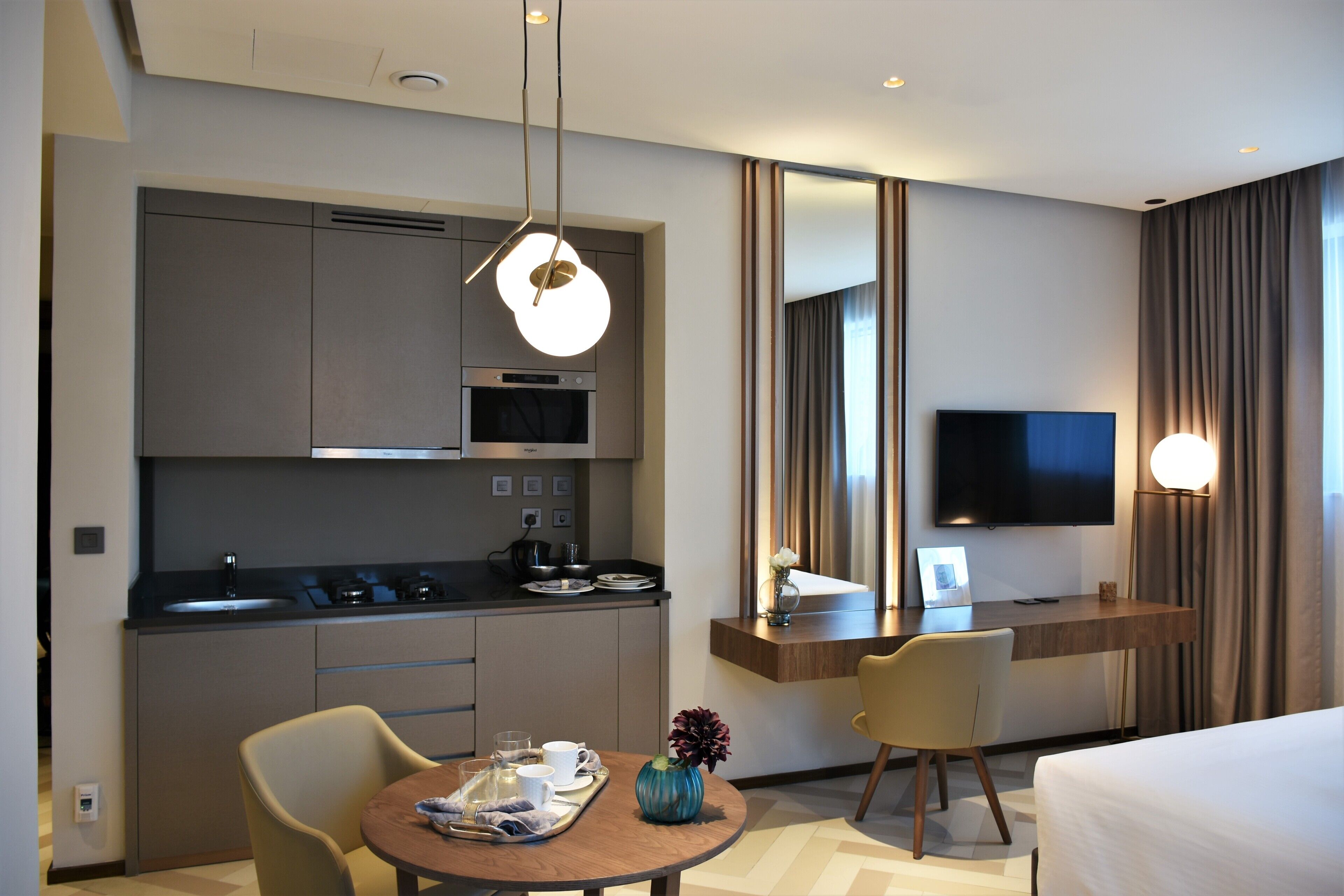 Una habitación de hotel moderna con kitchenette, zona de comedor, televisor y cama.