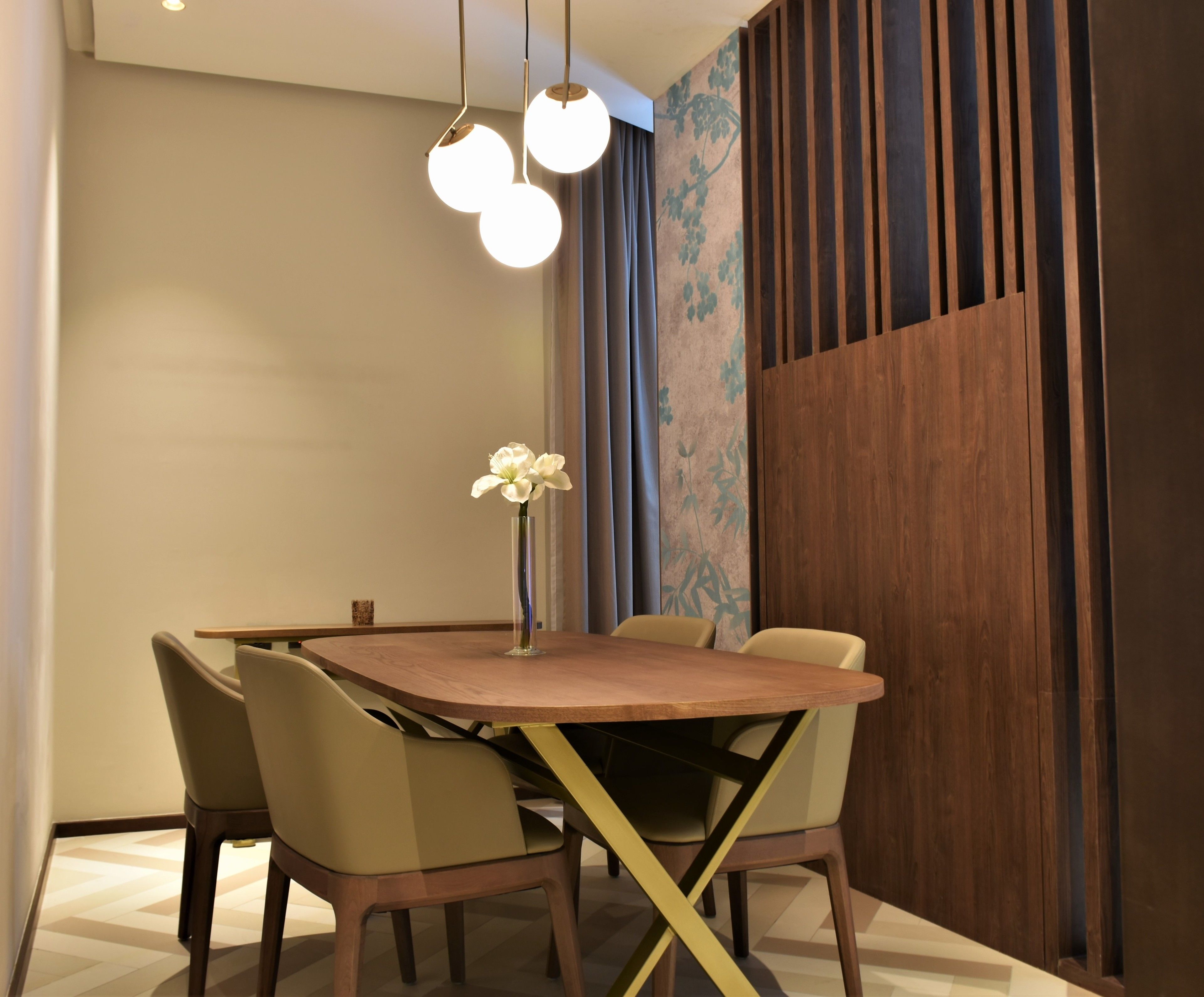 A dining area with a wooden table, four chairs, a vase with flowers, and a wall with vertical wooden slats and a floral pattern.