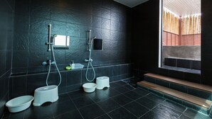 Un bagno moderno con pareti piastrellate di nero, una doccia, due servizi igienici e una finestra vista bambù.