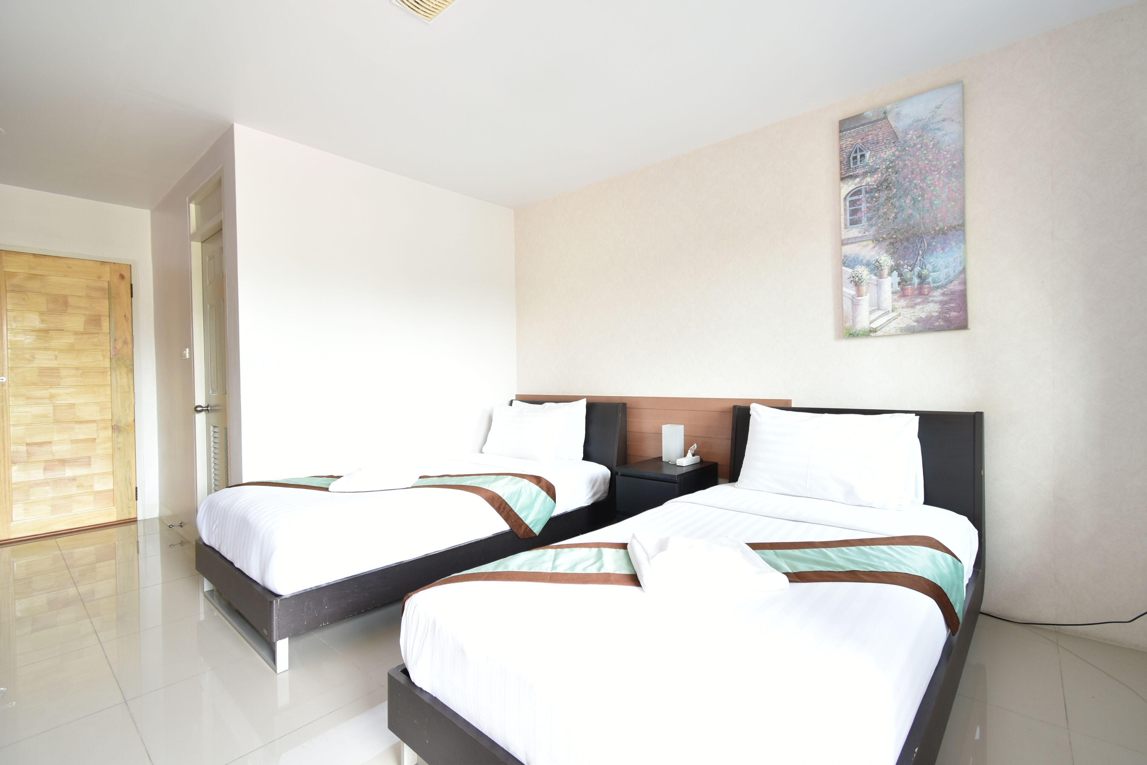 A hotel room with two beds, a wooden door, a painting on the wall, and a white ceiling.