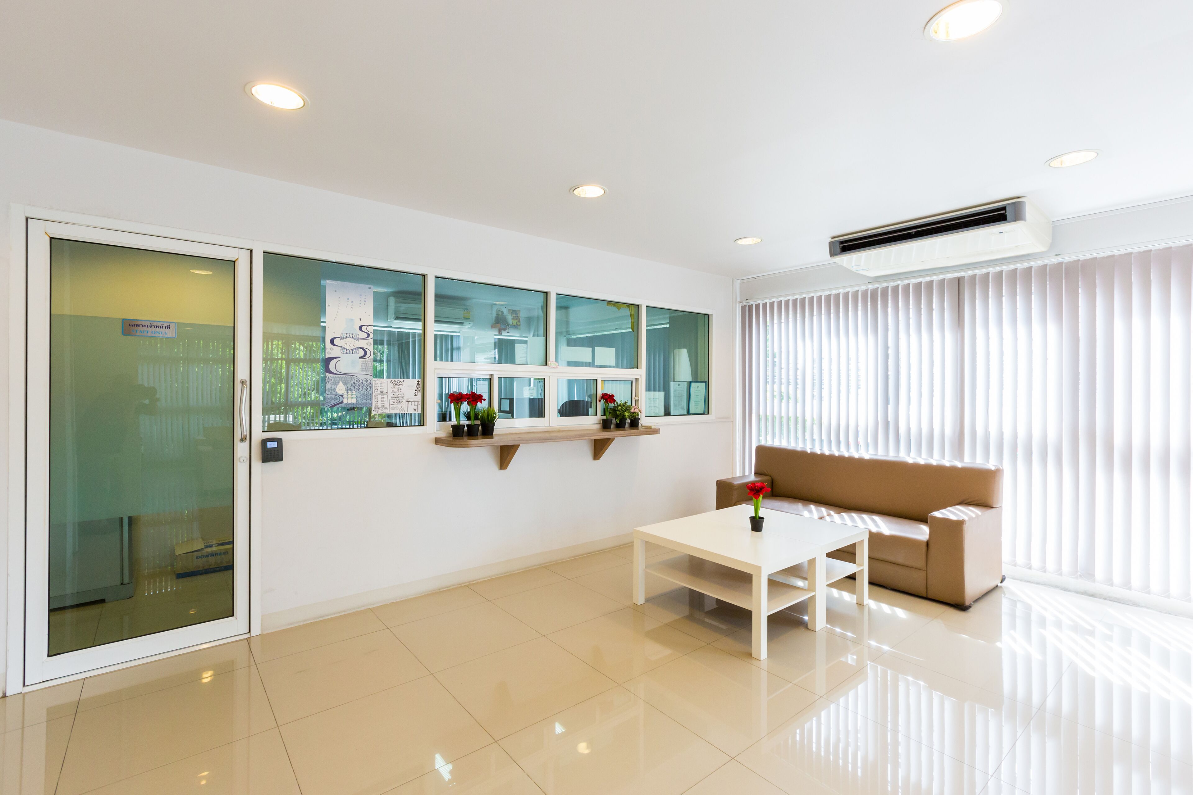 A modern, well-lit room with a beige sofa, a white coffee table, and a window with blinds.