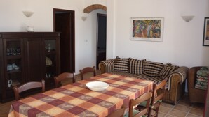 Un'area pranzo con tovaglia a quadri, sedie di legno, un divano e un mobiletto con vetri.