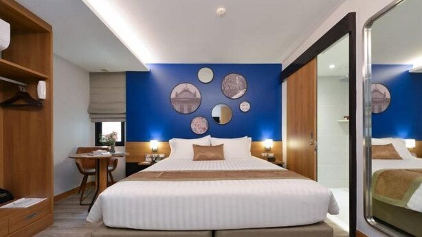 A hotel room with a large bed, a desk, and a chair. There are wall decorations and a mirror. - Aspira One Sutthisan (Bangkok)