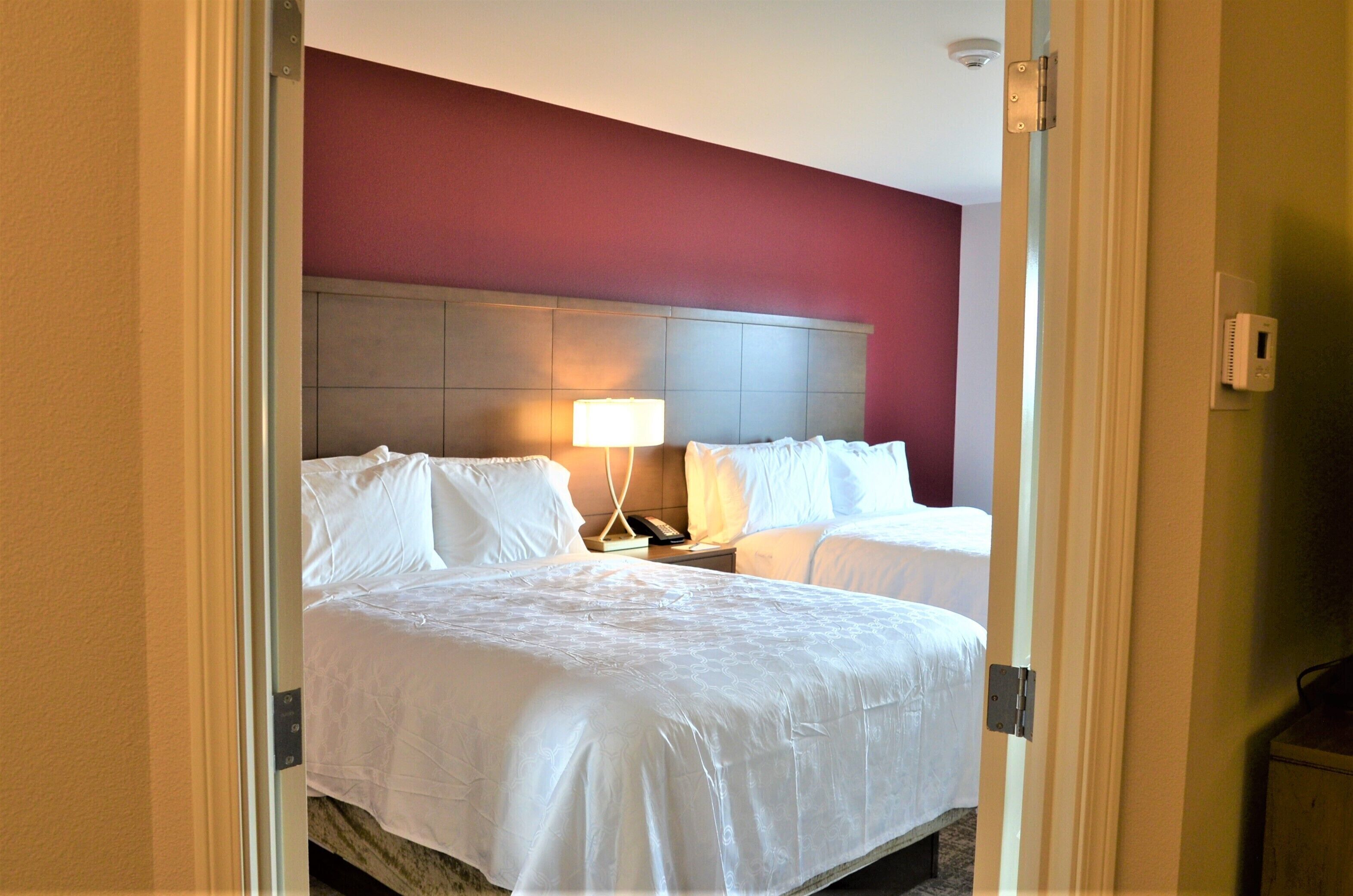 Une chambre d’hôtel avec deux lits, une table de chevet avec une lampe et un thermostat fixé au mur.